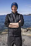 Mann ved kysten med Helly Hansen-lue og vest foran hav og fjell.