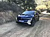 Mørk Renault Megane E-Tech står på en grusvei ved en skråning med trær og busker.